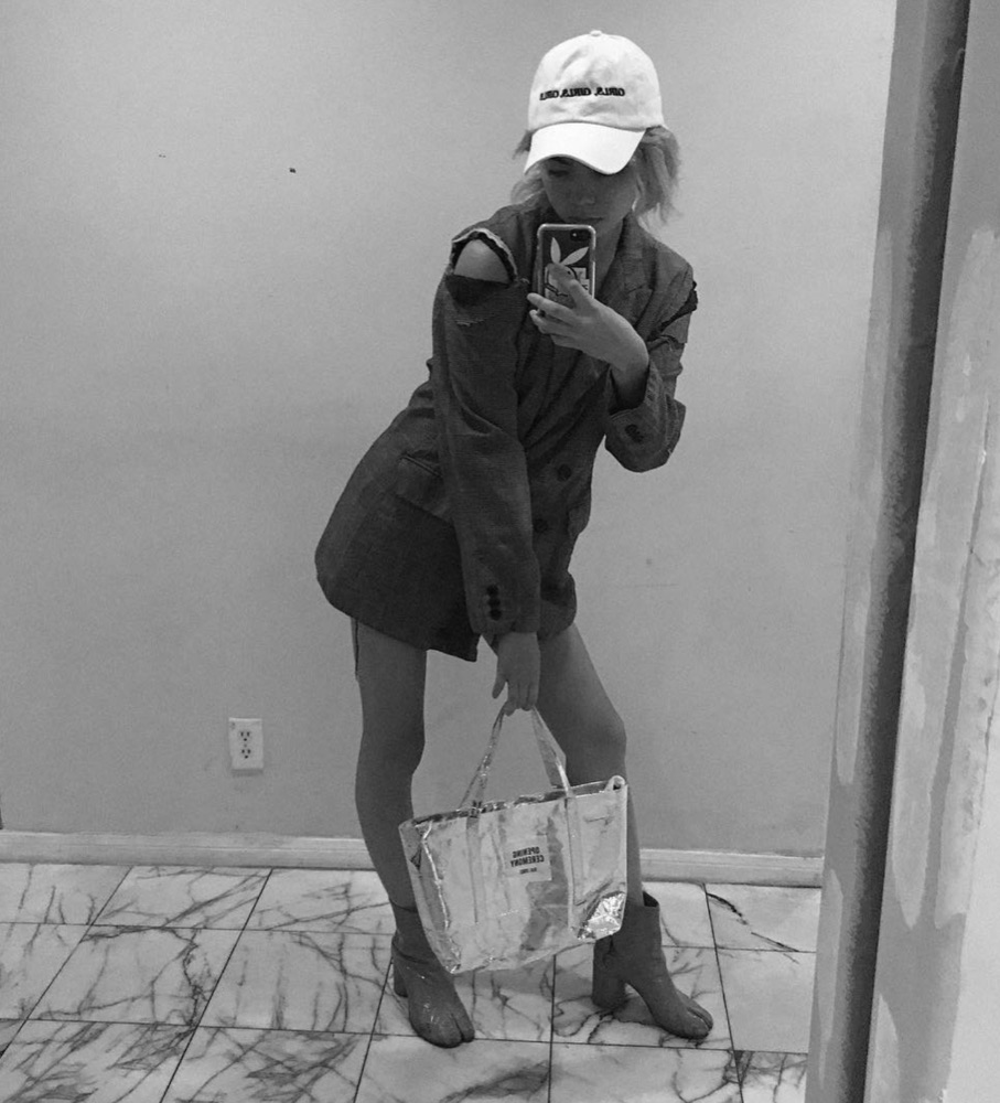 Black-and-white mirror selfie: cap with mirrored embroidery, deconstructed blazer dress with a cut-out shoulder, clear PVC tote and clear PVC boots on a marble floor