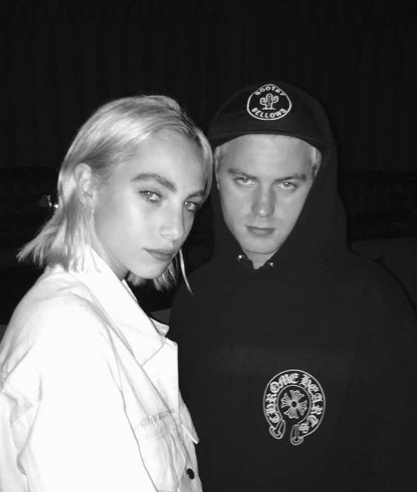 Black-and-white flash photograph at night: two people, one in a white jacket, one in a black hooded sweatshirt and cap