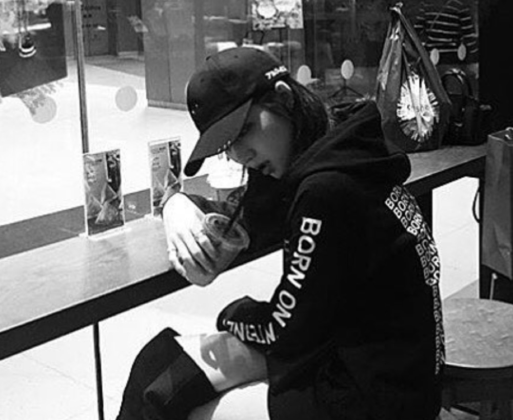 Black-and-white photograph: person at a mall food-court counter in a cap and a black hoodie printed BORN ON INTERNET down the sleeve, holding an iced drink