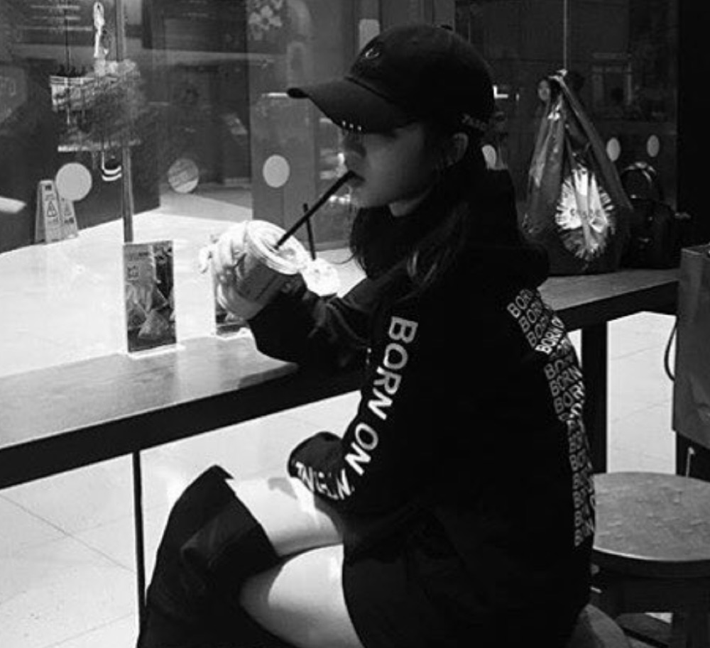 Black-and-white photograph: the same mall counter from a second angle, the drink raised, shopfront glass reflecting behind