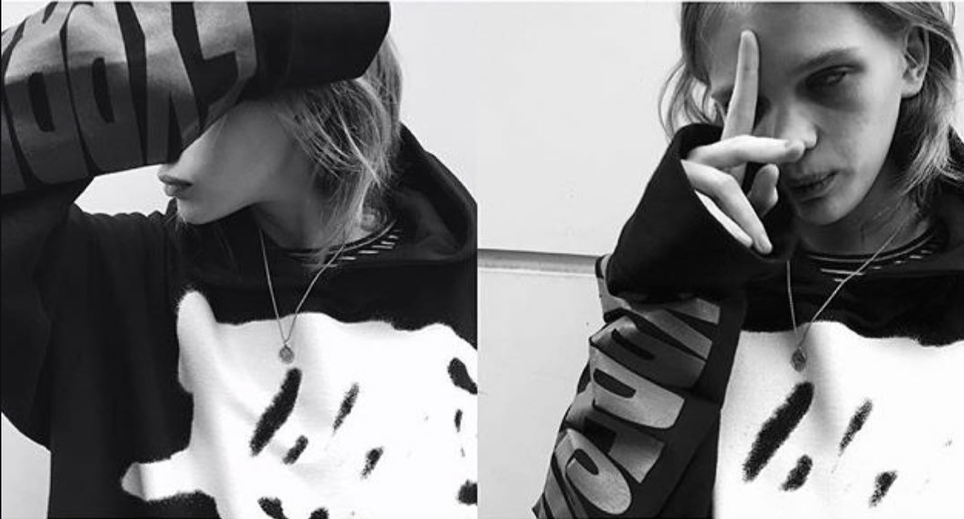 Black-and-white diptych: two frames of the same model in an oversized logo hoodie over a brush-marked white sweater, the second with a hand raised across the face