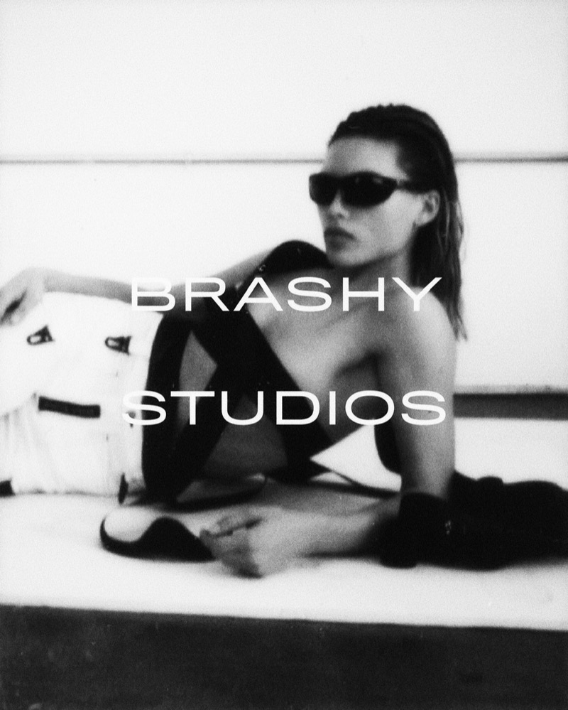 Black-and-white lookbook photograph with Brashy Studios type set over the frame, model reclined on a white bench