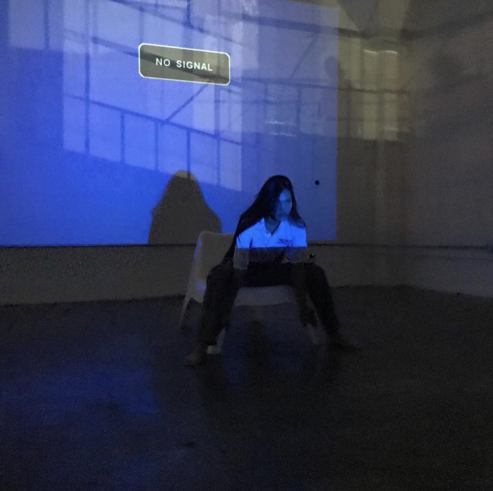 Studio floor in blue projector light: a NO SIGNAL bar thrown across the wall, a seated model lit by the same beam